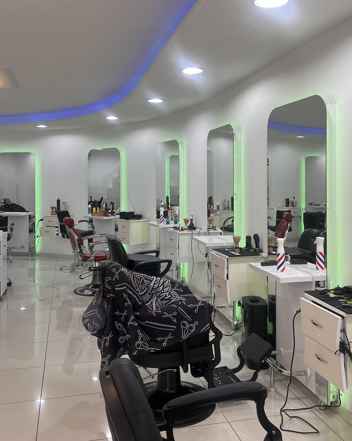 Het interieur van Barbershop Babylon: witte zaak met een blauwe lichtlijn in het plafond en een rij boogspiegels met groen licht langs de kappersstoelen